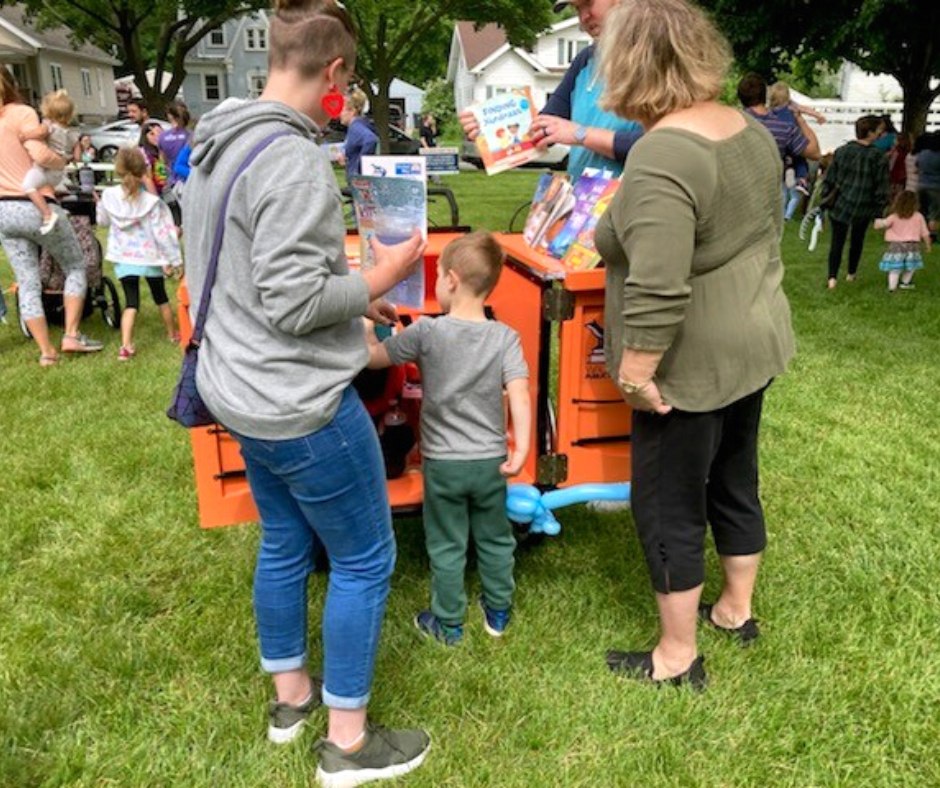 Several people stand in front of orange Book Bike, looking into it and holding books