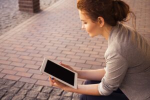 A women reading on a tablet outside on a sidewalk
