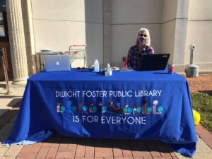 A woman sitting behind a table that has the phrase "Dwight Foster Public Library is for Everyone" printed on its table cloth