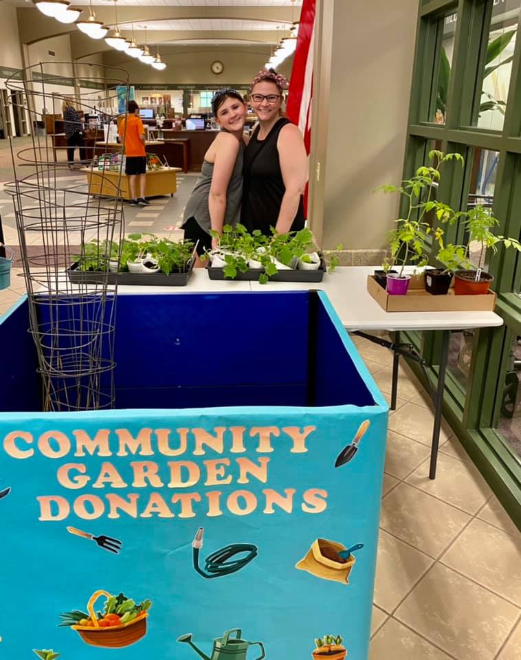 Two people posing behind a box that says "Community Garden Donations"