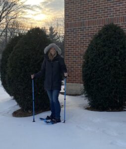 A woman posing outdoors in the snow wearing snowshoes she checked out from the library