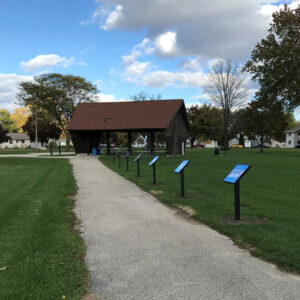 Photo of a path with StoryWalk sign holders along a path leading to a park shelter building.