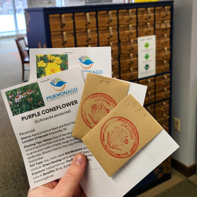 Hand holding seeds in front of the Mukwonago Seed Library
