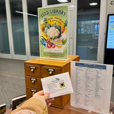 Hand holding a seed packet in front of the Waukesha Seed Library